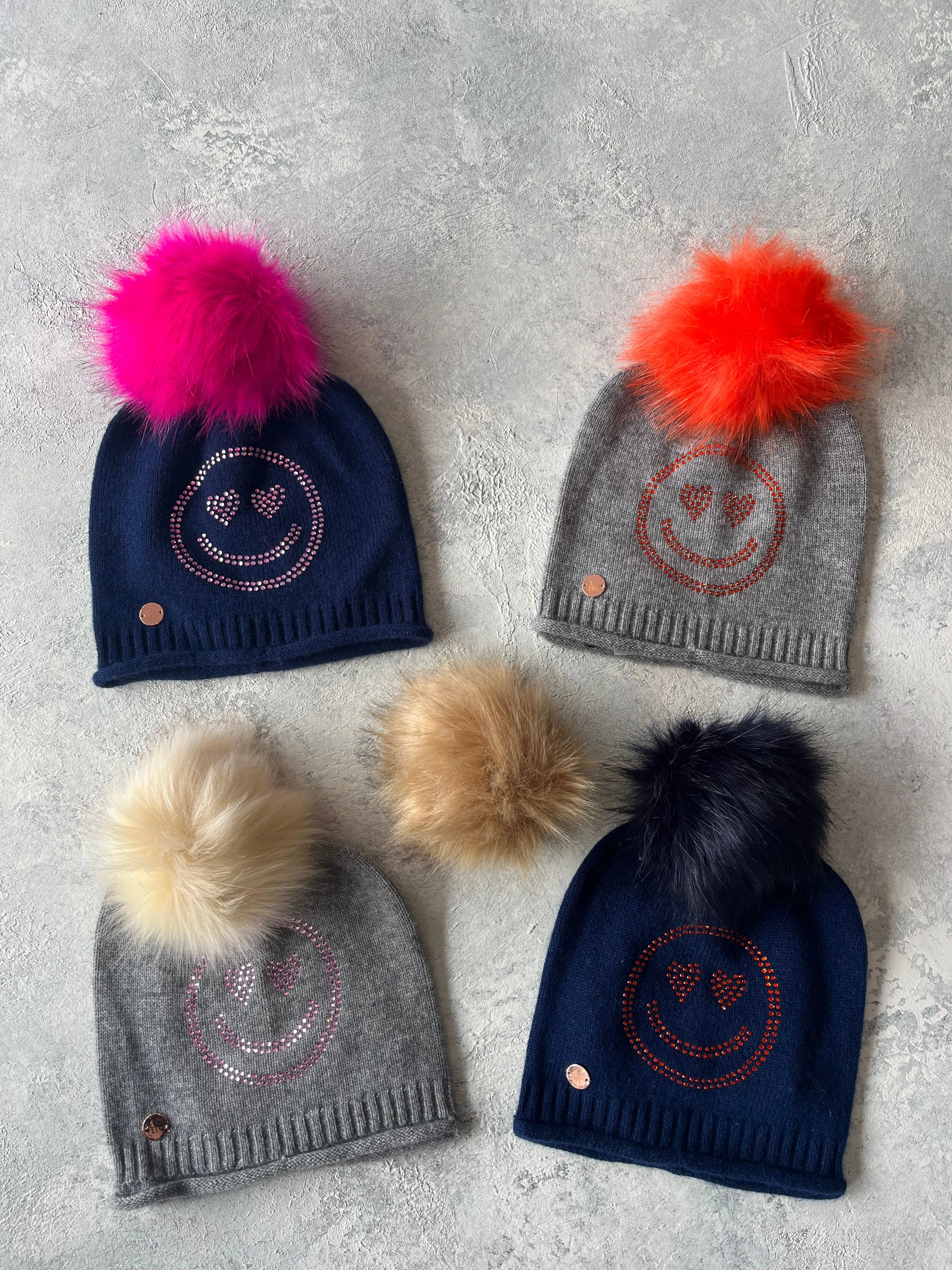 Navy cashmere plain knit beanie with an orange smiley embellishment & faux fur pom